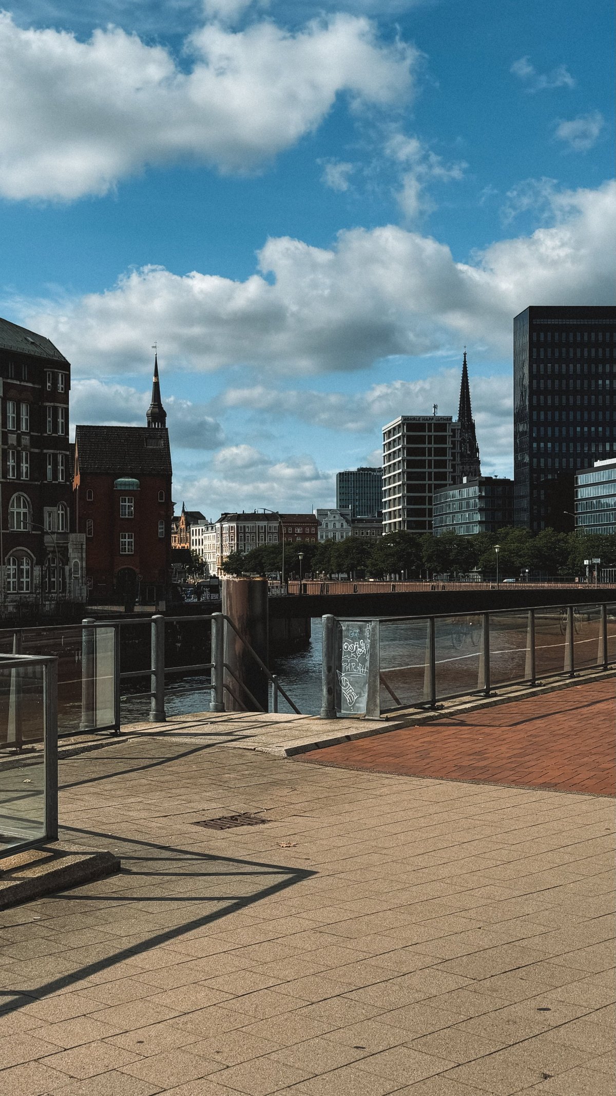 Dortmunder Uferpromenade am Kanal mit Backsteinpflaster, Geländer, historischen Kirchen und modernen Gebäuden unter blauem Himmel